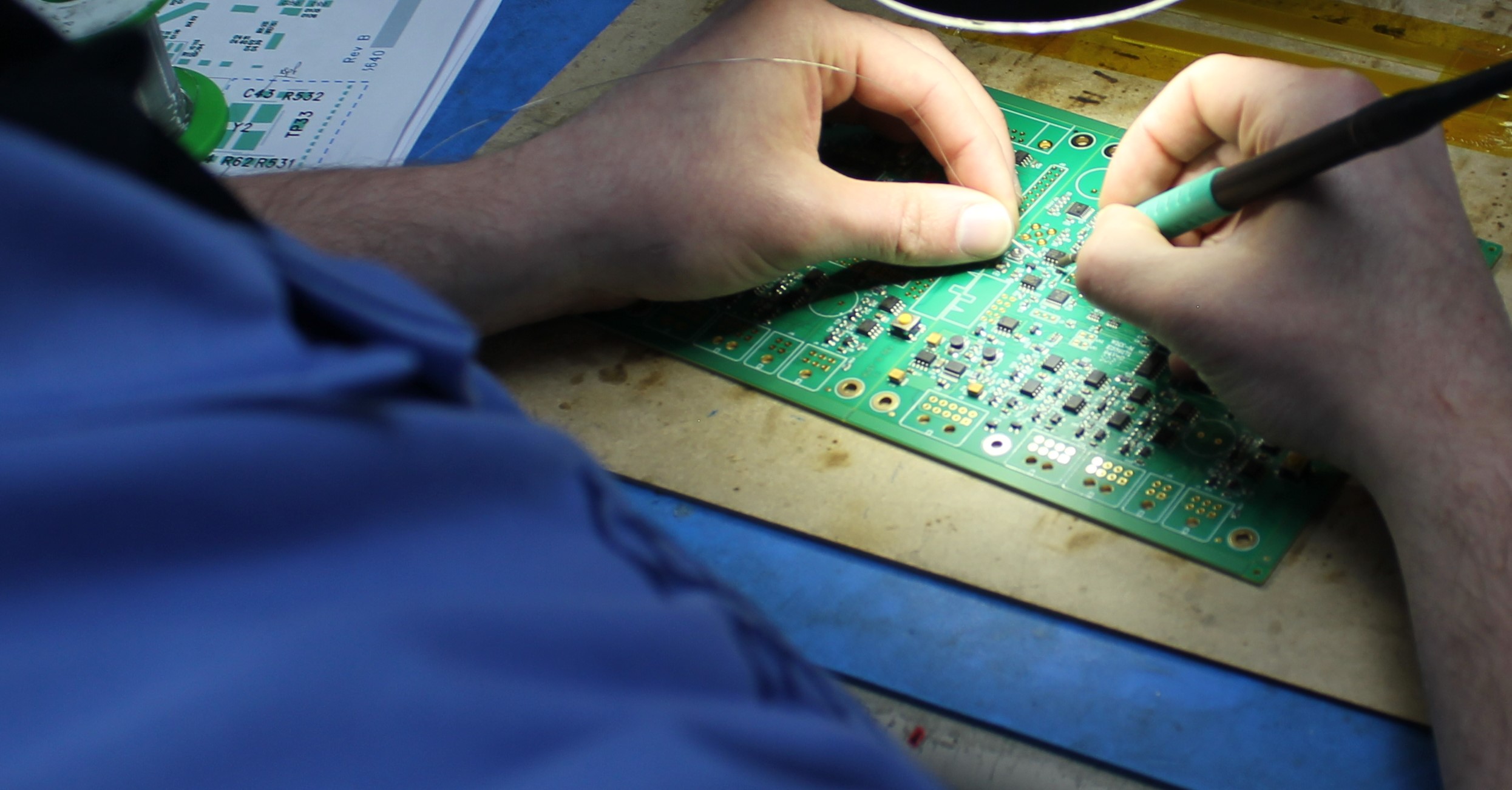 An image of an operator soldering a surface mount component to a printed circuit board using a soldering iron